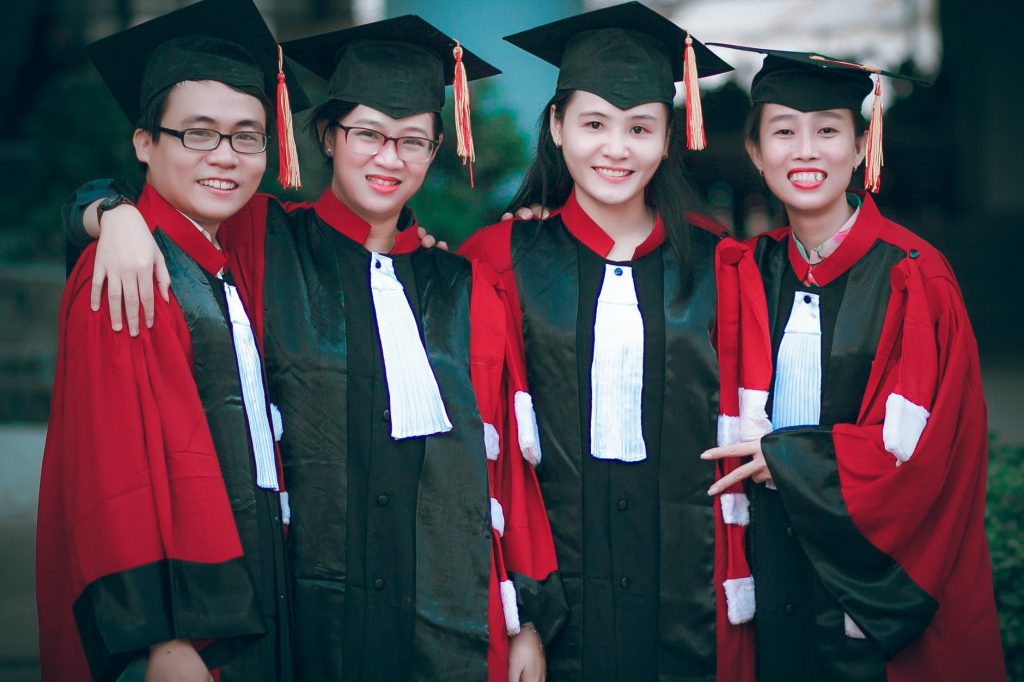 man and women wearing red and black academic gowns and black mortar boards