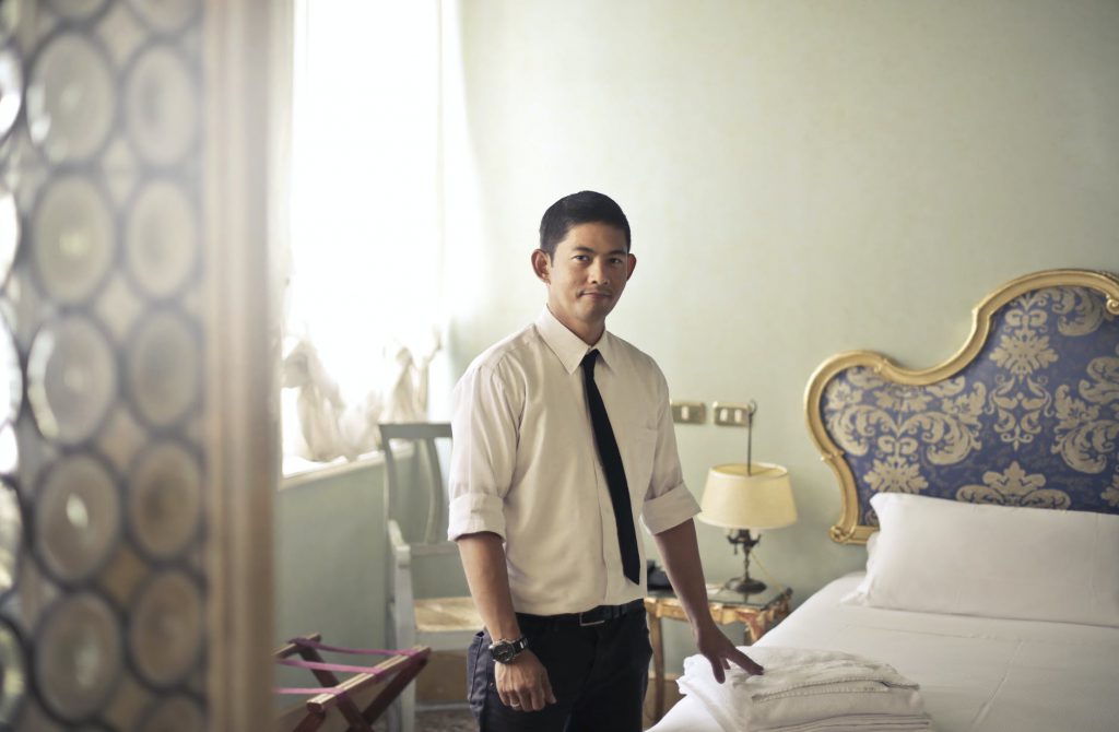 ethnic male maid arranging hotel room