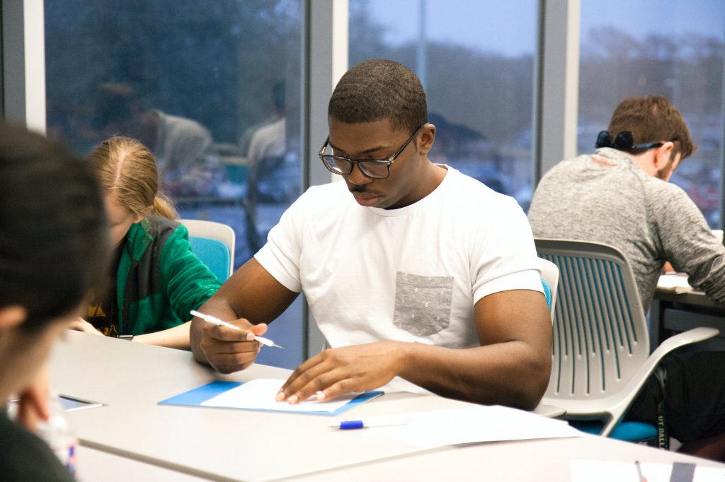 man in white crew neck t shirt sitting on chair while holding white pen